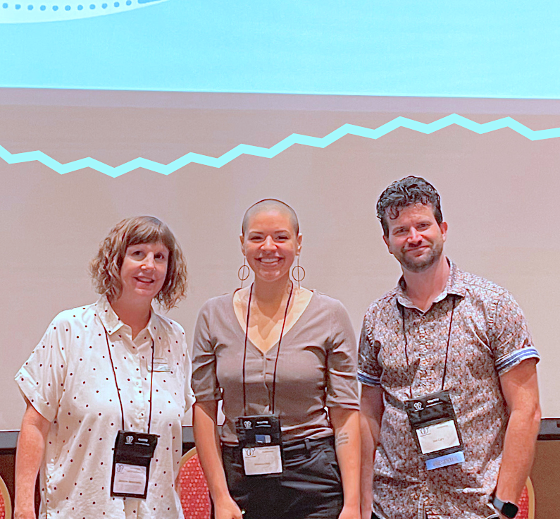 Jacquie, Monica, and Joe stand in front of a slideshow presentation about Autistic burnout. 